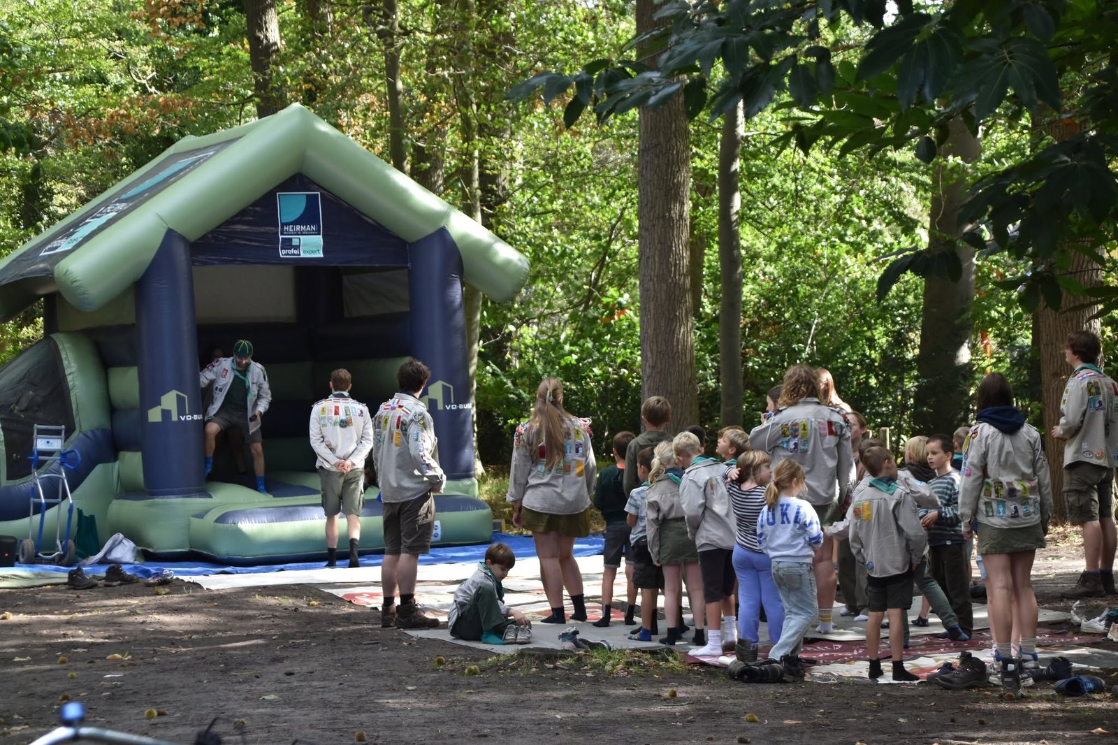 Kinderen en leiding in uniform bij een springkasteel in den bos van Scouts Sinaai